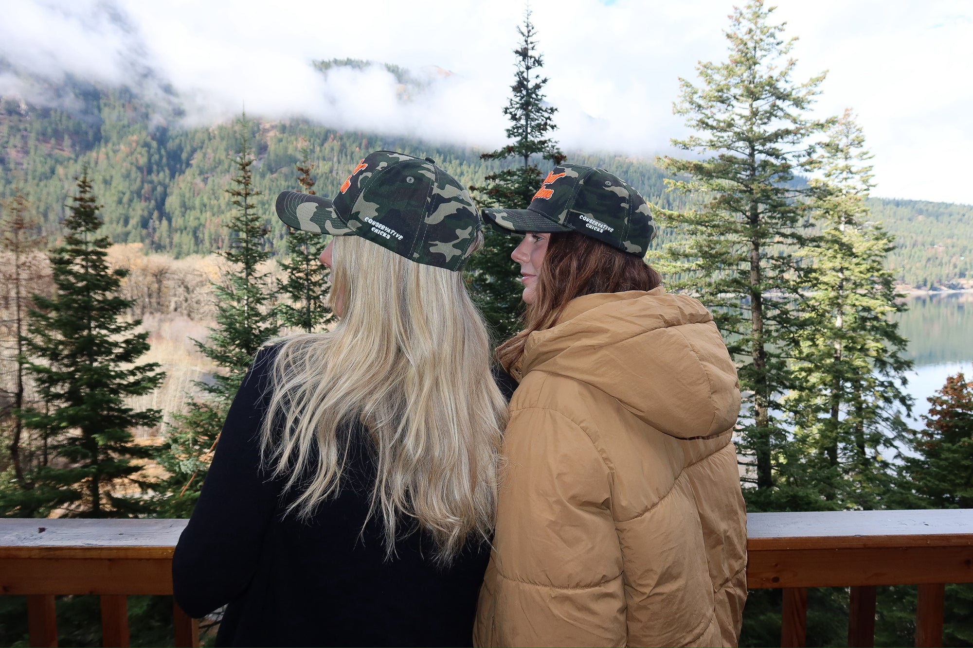 Two people wearing camo hats with a scenic view of trees and water in the background