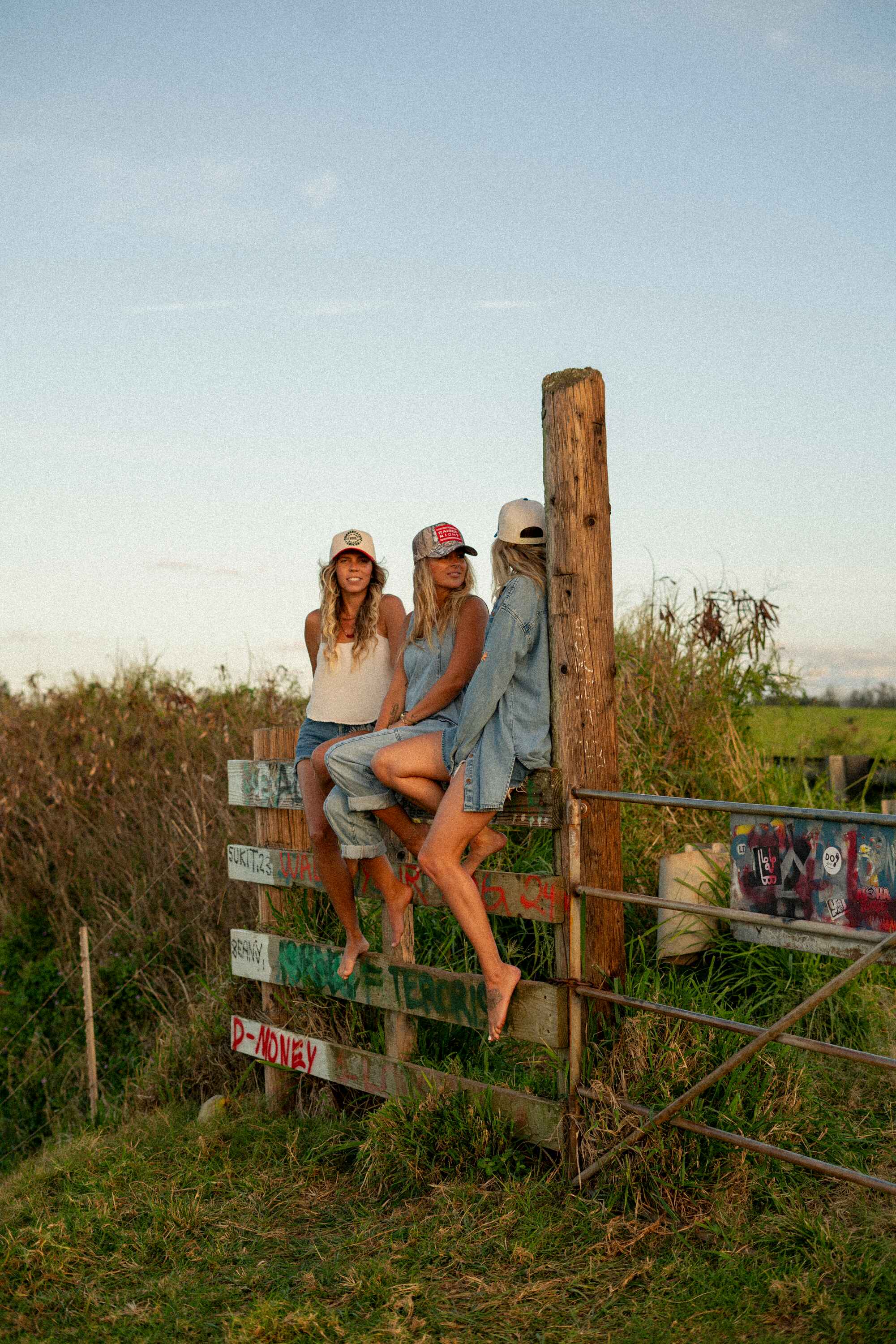 3 girls sitting on a fence wearing baseball caps