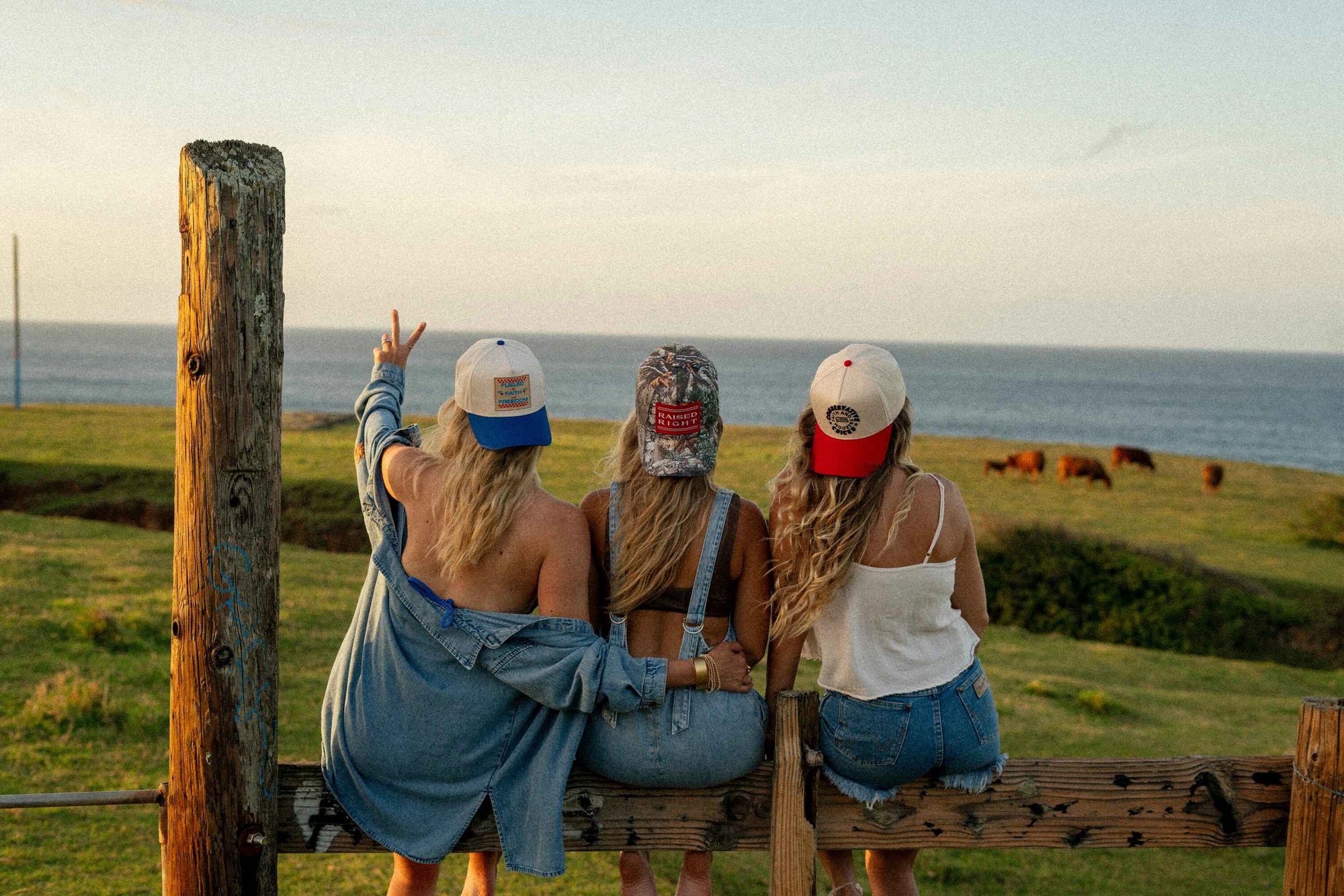 3 girls sitting on a fence wearing hats backwards