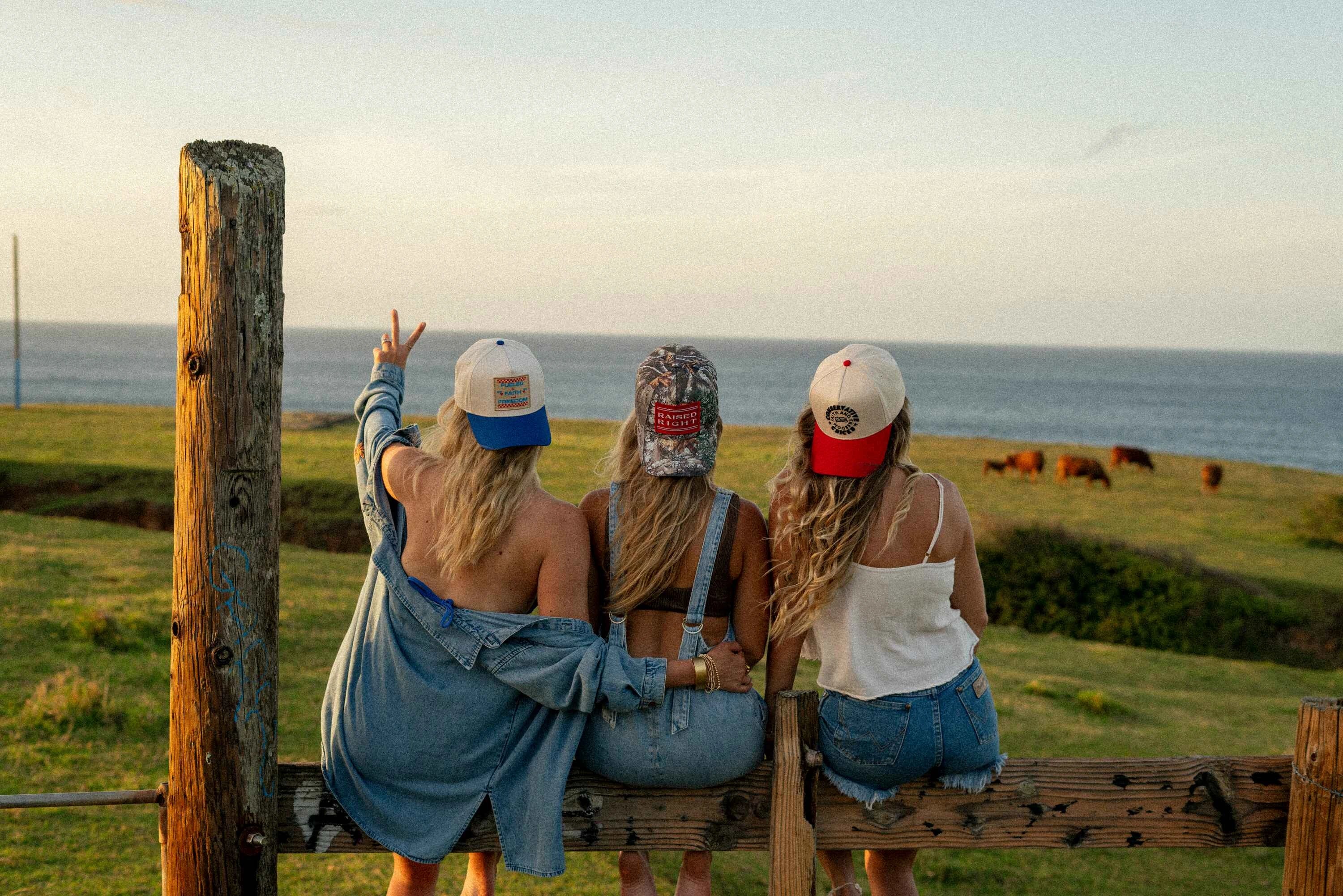 3 girls sitting on a fence wearing hats backwards